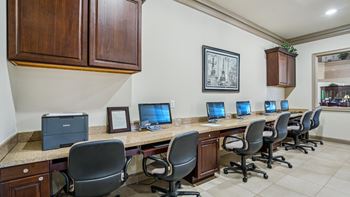 A row of computers are on a desk in a room with wood paneling.